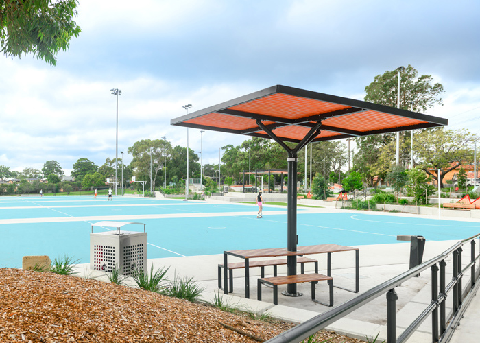 ChillOUT Tree (CT1) powered, in Satin Monument with custom roof colour (Red Dust). Linea Table (LIT10-DDA, 1900mm) and Linea Bench (LIB6) in aluminium woodgrain Spotted Gum battens and Textura Monument frame.