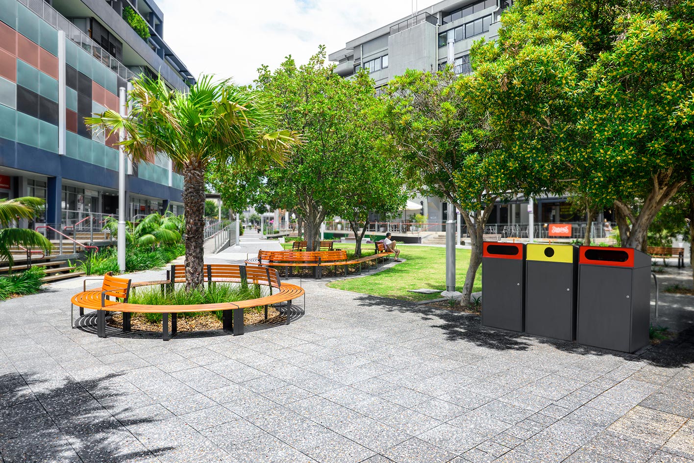 Curved Linea Seats and Benches with frames in Textura Monument, battens in Bistro Orange and aluminium woodgrain Spotted Gum. Escola Bin Enclosures in Textura Monument.