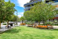 Curved and straight Linea Seats and Benches with frames in Textura Monument, battens in Bistro Orange and aluminium woodgrain Spotted Gum. Escola Bin Enclosures in Textura Monument.