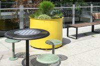 Cafe Table in Dark Bronze Textura with chess board, Cafe Stools in Pale Eucalypt. Frame Planter Round XL in Mustard Satin and Linea VT Bench.