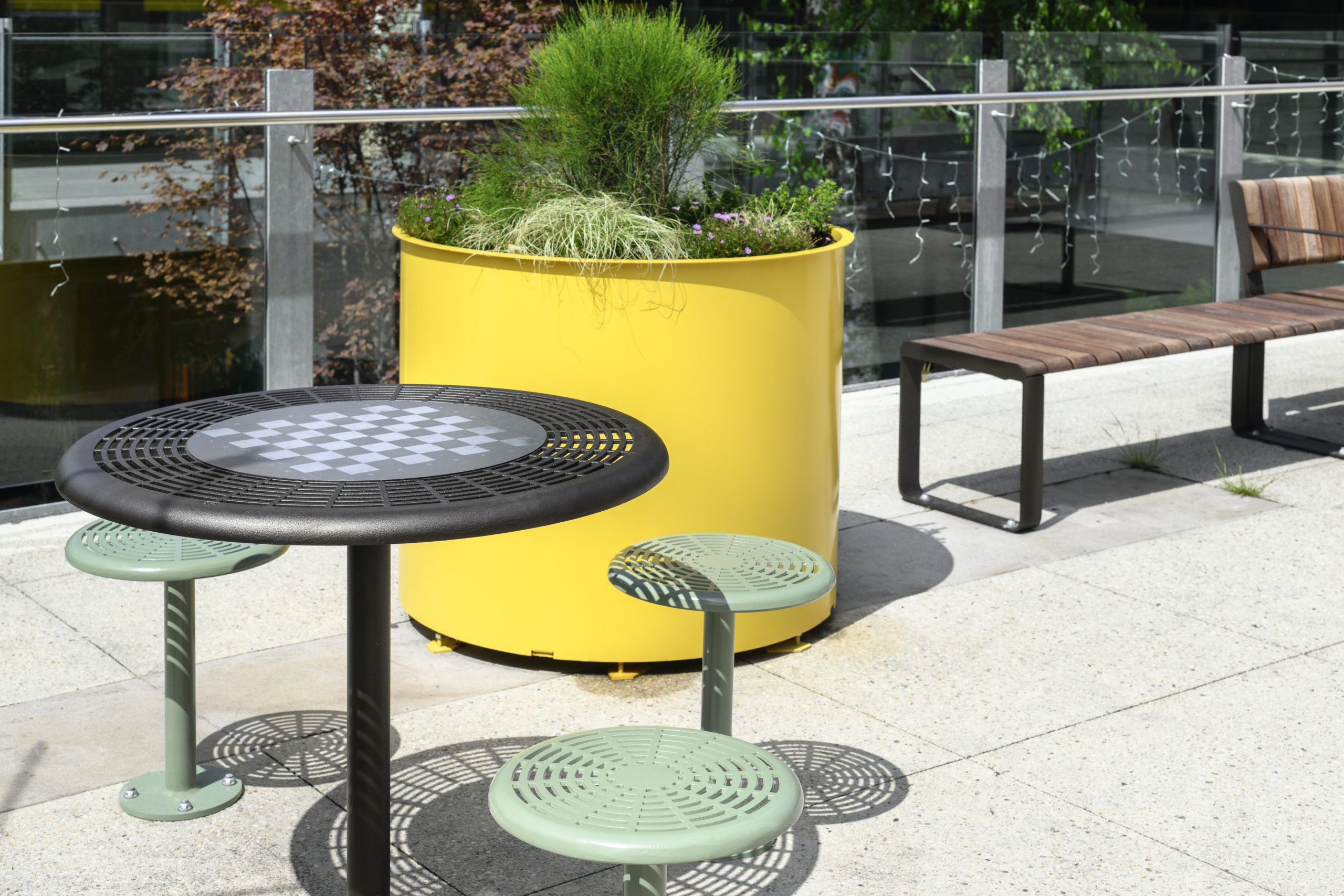 Cafe Table in Dark Bronze Textura with chess board, Cafe Stools in Pale Eucalypt. Frame Planter Round XL in Mustard Satin and Linea VT Bench.