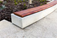 Linea Curved Bench, plinth-fixed, tailored internal radius, aluminium woodgrain Spotted Gum battens, Textura Russet frames.